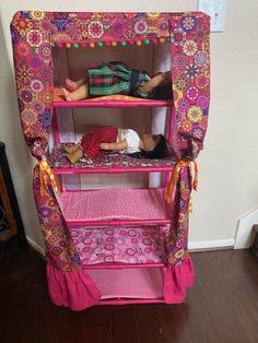 two dolls laying on top of a pink doll house with flowers and polka dot curtains