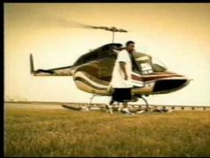 a man standing next to a helicopter on top of a grass covered field in front of a sky