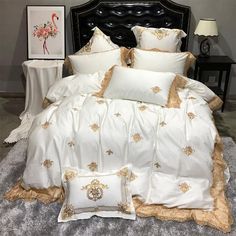 a bed with white and gold comforters in a room next to a lamp on a table