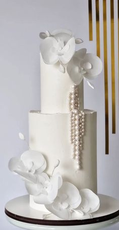 a three tiered white wedding cake with flowers and pearls on the side, sitting on a plate