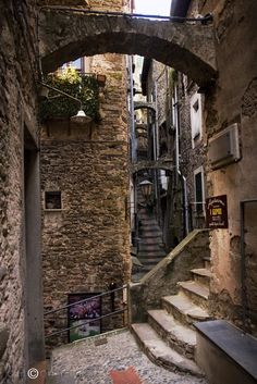 an alleyway with stone steps and stairs leading up to the second floor, surrounded by old buildings