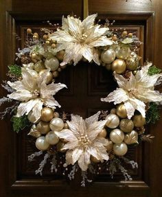 a christmas wreath with white flowers and gold baubles hanging from the front door