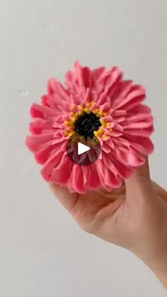 a hand holding a pink flower with a black center and yellow center in the middle