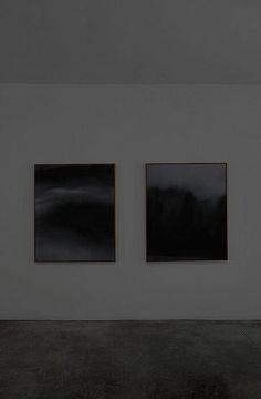 three black and white paintings hanging on the wall in an empty room with concrete flooring