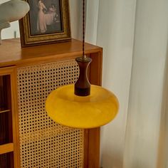 a yellow lamp hanging from the ceiling next to a wooden cabinet with pictures on it