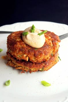 two crab cakes on a white plate with a knife and fork next to it, topped with sour cream