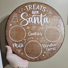 a hand holding a wooden sign that says treats for santa cookies milk reindeer carrots