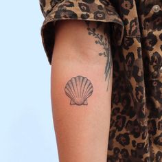 a woman's arm with a small shell tattoo on the left side of her arm