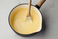 a wooden spoon in a saucepan filled with yellow liquid on a white counter top