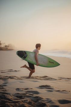 a young man running on the beach with his surfboard in hand, carrying it