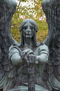 an angel statue with its arms crossed and hands folded over it's face, in front of trees