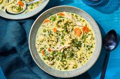 two bowls of chicken noodle soup on a blue tablecloth next to silverware