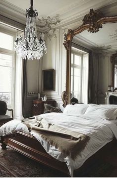 a large bed sitting in a bedroom next to a window with a chandelier hanging from the ceiling