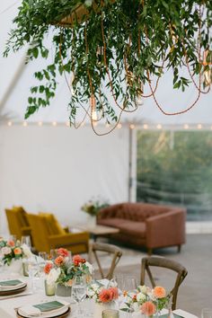 the table is set with place settings and flowers on it, along with greenery hanging from the ceiling