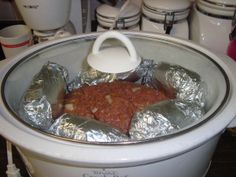 a slow cooker with foil wrapped around the lid and meat in it, ready to be cooked