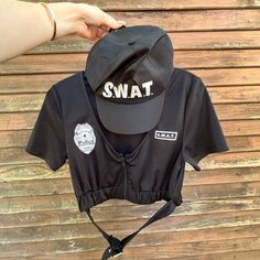 someone is holding onto a black shirt with the word swat on it and a hat attached to it