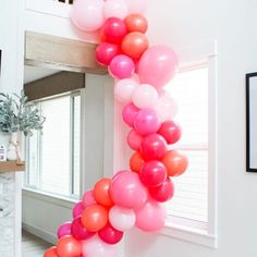 a bunch of pink and orange balloons hanging from the ceiling in a room with white walls