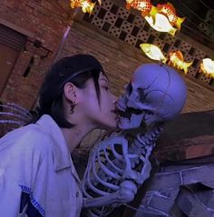 a woman kissing a skeleton in front of a brick wall