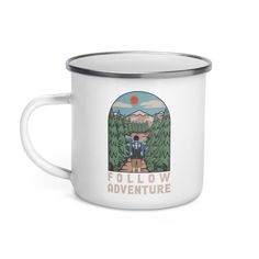 a white enamel mug with the words follow adventure printed on it and two people walking down a path