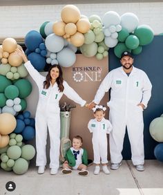 a man and woman holding hands while standing next to two children in front of balloons