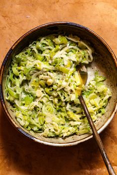 a bowl filled with shredded green vegetables on top of a wooden table next to a spoon