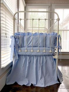 a white metal crib with blue bedding and pillows on the bottom row, in front of windows