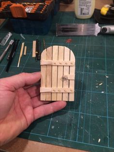 a person holding a piece of wood in their hand next to other tools on a table