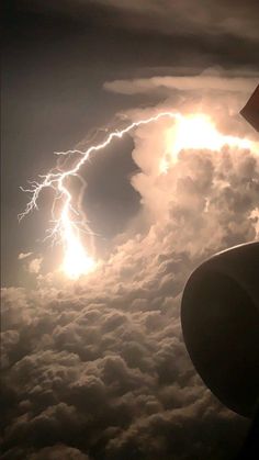 the view from an airplane window shows lightning in the sky above clouds and a plane wing