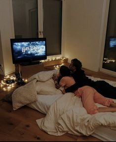 two people laying on a bed in front of a tv