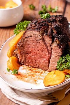 a white plate topped with meat and potatoes on top of a wooden table next to a bowl