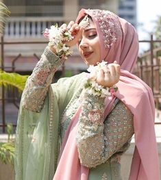 a woman wearing a hijab and holding flowers in front of her face with both hands