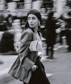 a woman walking down the street while wearing a coat and holding a cup in her hand