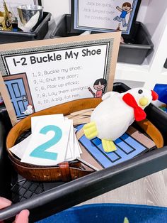 a child's hand holding a toy chicken in front of a sign that says, i - 2 buckle my shoe