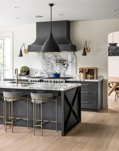 a kitchen with marble counter tops and black cabinets, gold bar stools and pendant lights