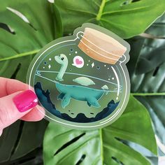 a hand holding up a sticker with an image of dinosaurs in a jar