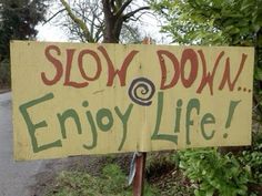 a sign that says slow down enjoy life on the side of a road with trees in the background