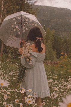 a woman holding an umbrella standing in a field of daisies and wildflowers