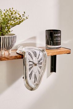 a glass clock on a shelf next to a potted plant and candle in a black and white striped vase