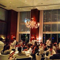 people sitting at tables in a restaurant with chandelier hanging from the ceiling and windows