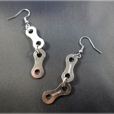 two pairs of silver metal earrings on a black surface