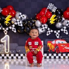 a baby boy sitting on the floor in front of a birthday cake backdrop with cars