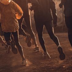 a group of people running down a dirt road next to each other in the sun