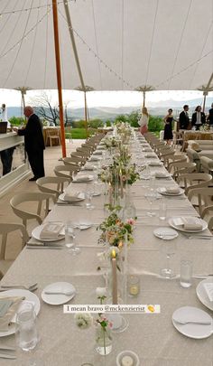 a long table is set up with white plates and place settings for an outdoor event