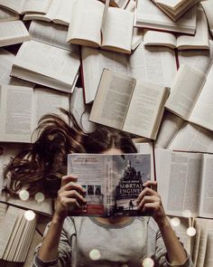 a woman laying on the ground reading a book with many books scattered around her and covering her face