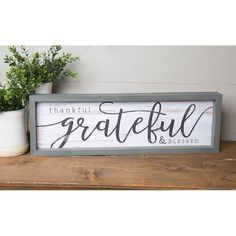 a wooden sign that says grateful and is sitting on a shelf next to potted plants