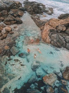 three people swimming in the ocean near some rocks