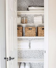 an organized closet with baskets and toilet paper on the shelves in black and white patterned wallpaper