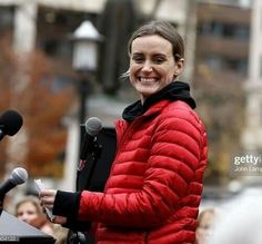 a woman standing at a podium with microphones in front of her and people behind her