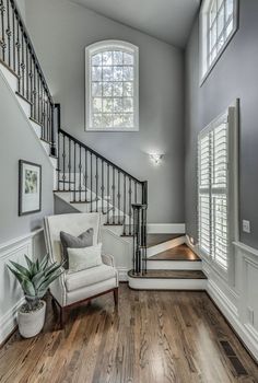 a white chair sitting under a window next to a stair case in a room with wooden floors