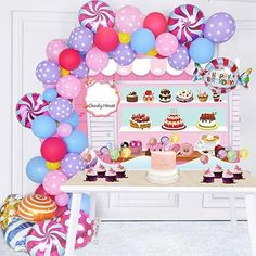 a table topped with lots of balloons and cake next to a wall filled with cakes